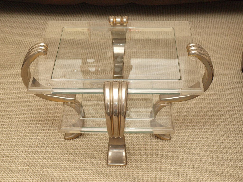 Pair two-tier tables with scrolling supports in chrome plated brass; the glass plateaux inset in lucite frames with routed outer edges